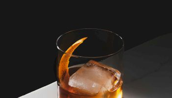 A glass of whiskey with a large ice cube sits on a marble surface, casting a warm glow in a minimalist setting.