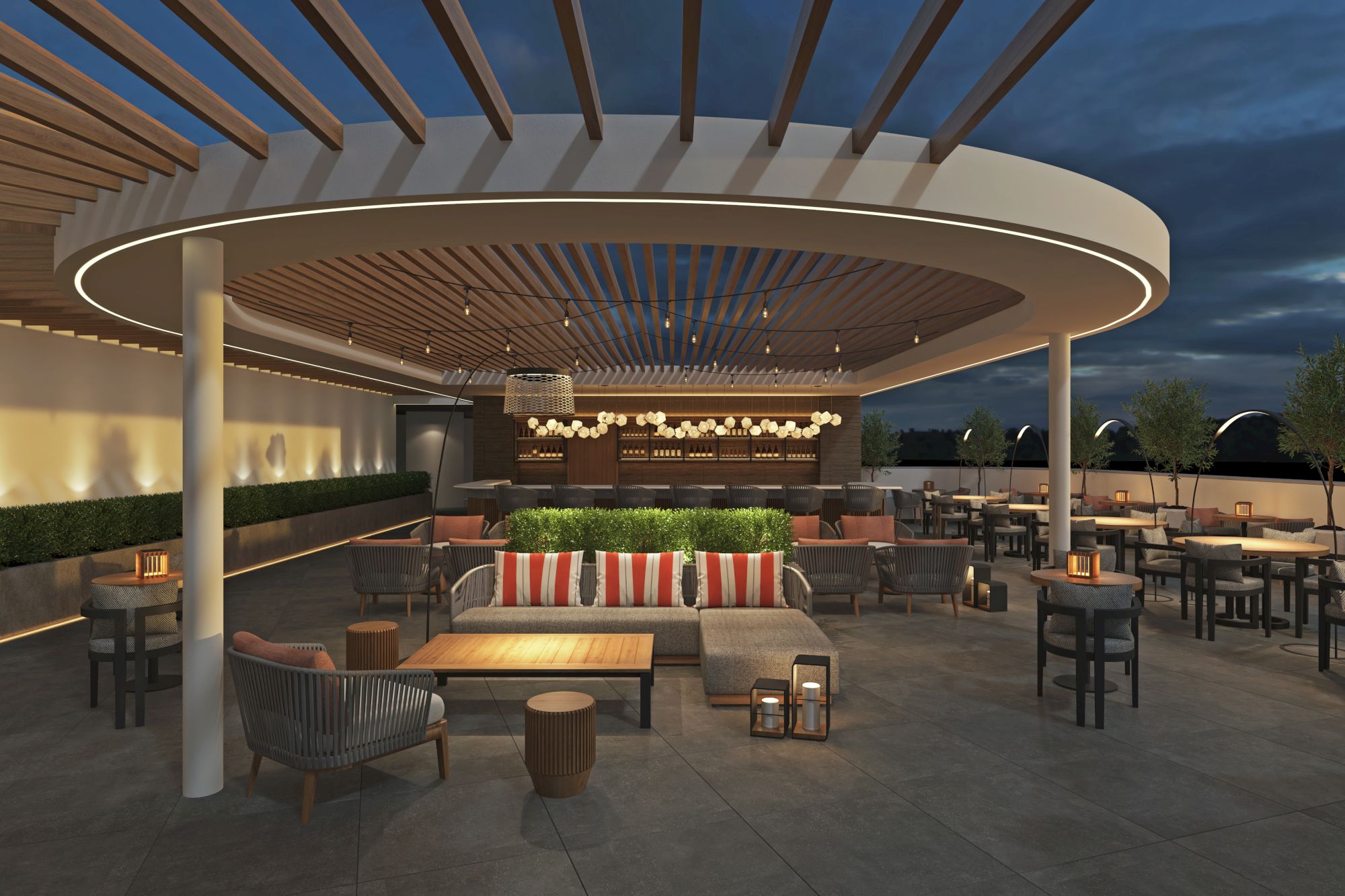A stylish rooftop lounge with a circular overhead canopy, modern seating, warm lighting, and a bar in the distance at dusk.