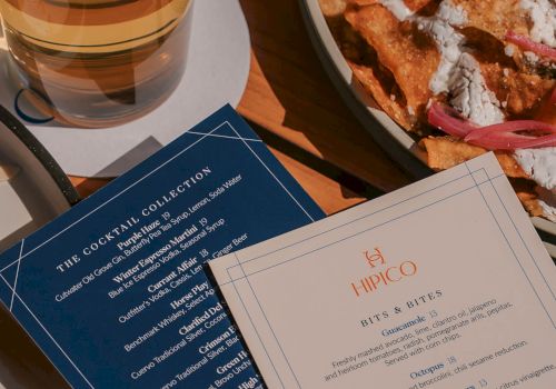 A beer glass beside a plate of nachos and two menus on a table.