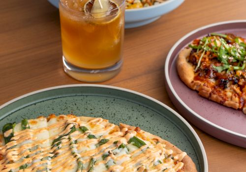 A table of food: pizza slices with creamy drizzle, a side salad, and a glass of orange juice with ice, on plates.