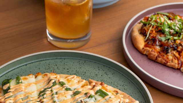 A table of food: pizza slices with creamy drizzle, a side salad, and a glass of orange juice with ice, on plates.
